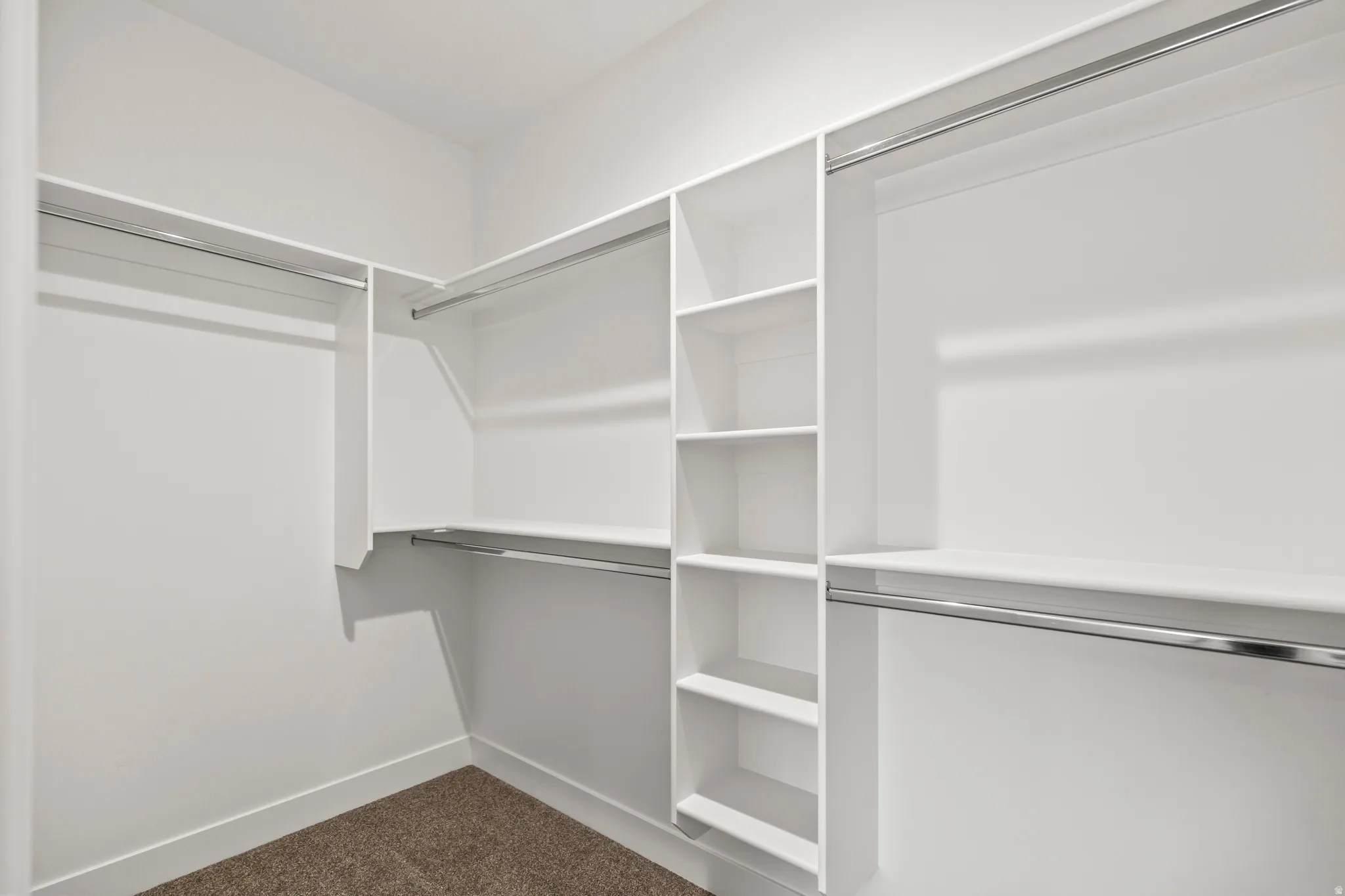 Built-in closet system with shelving, multiple hanging rods, and neutral carpet flooring