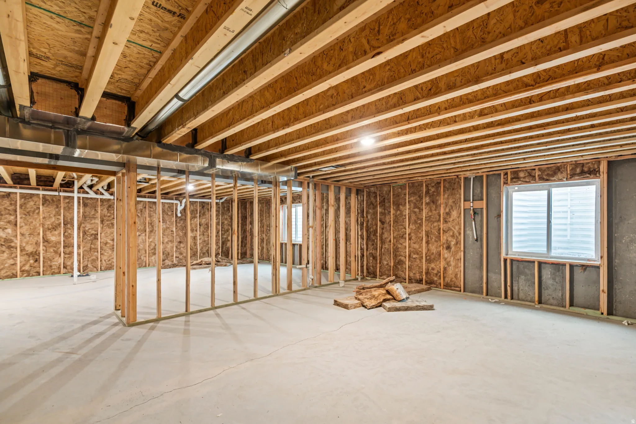 Unfinished basement featuring wood framing, exposed joists, concrete flooring, and an egress window