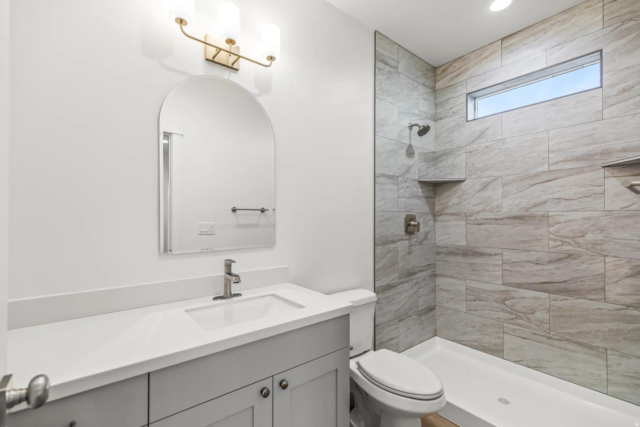 White vanity with a single basin sink and light gray cabinetry, complemented by an arched mirror and a three-light fixture