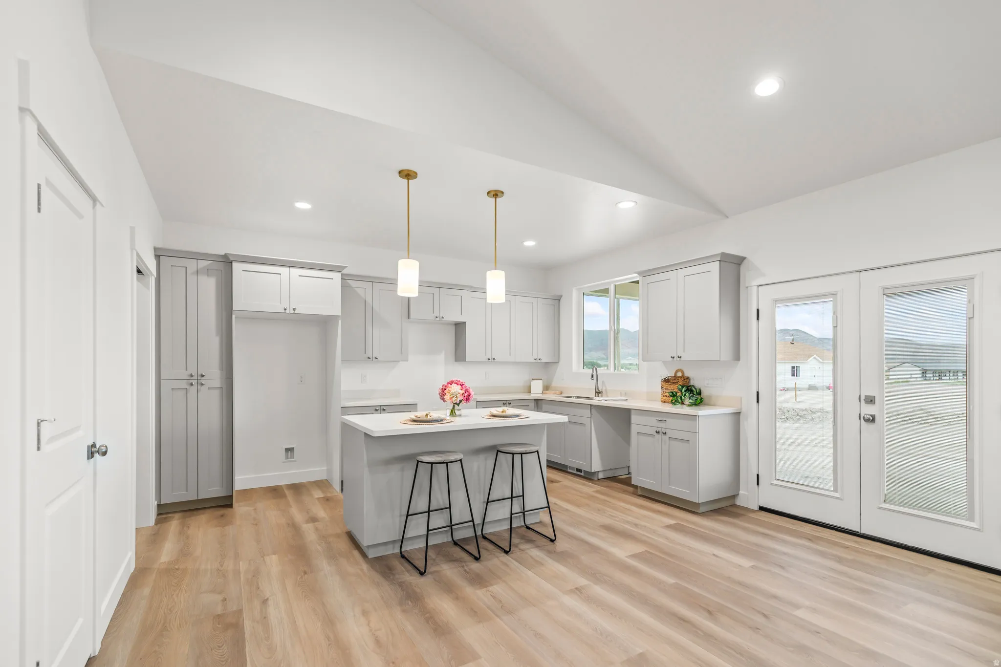 Modern kitchen featuring light gray cabinetry, white countertops, wood-finish flooring, a kitchen island with pendant lighting, and French doors to the exterior