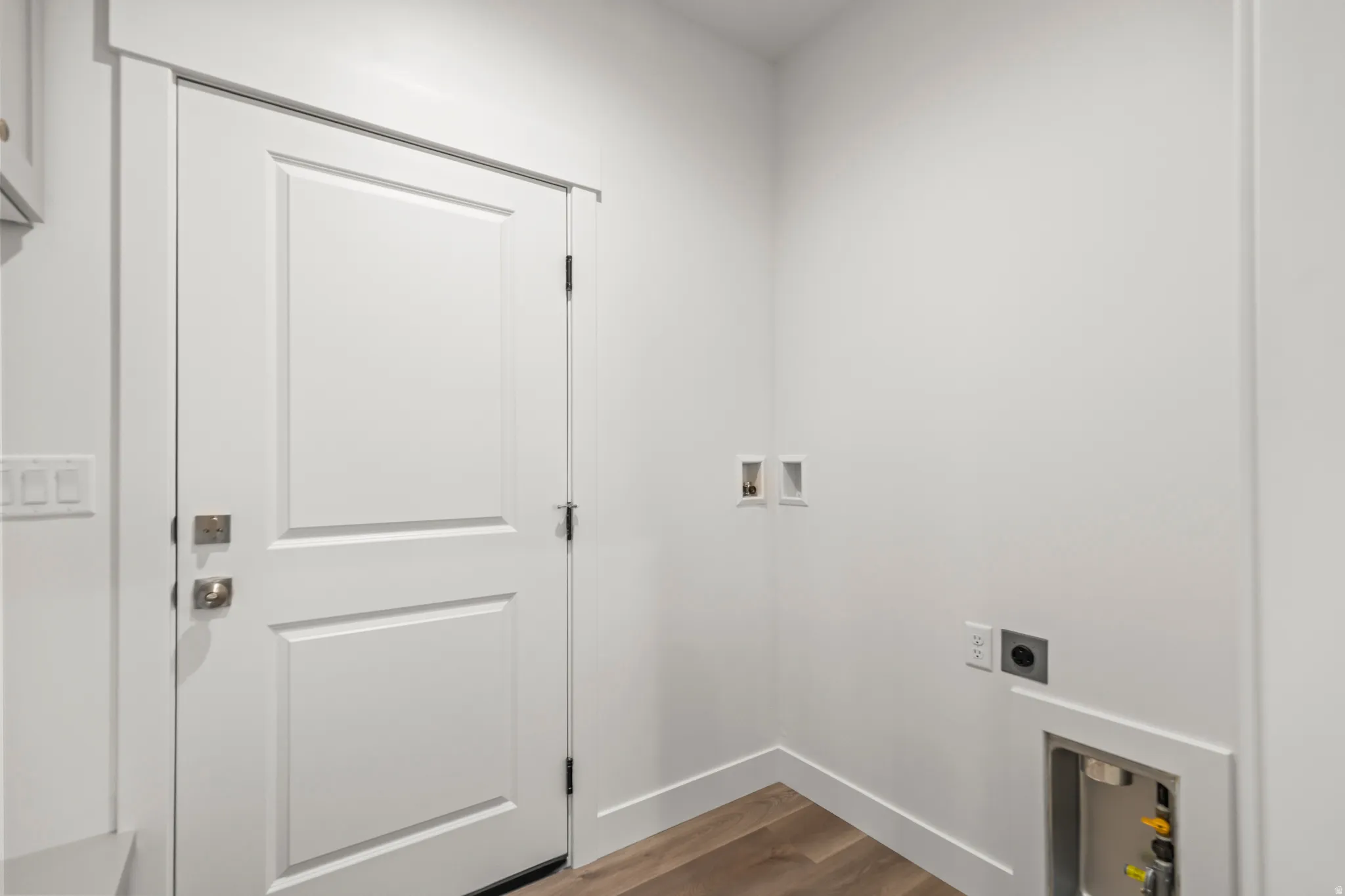 Wood-finish flooring, white walls, and a paneled door with brushed nickel hardware