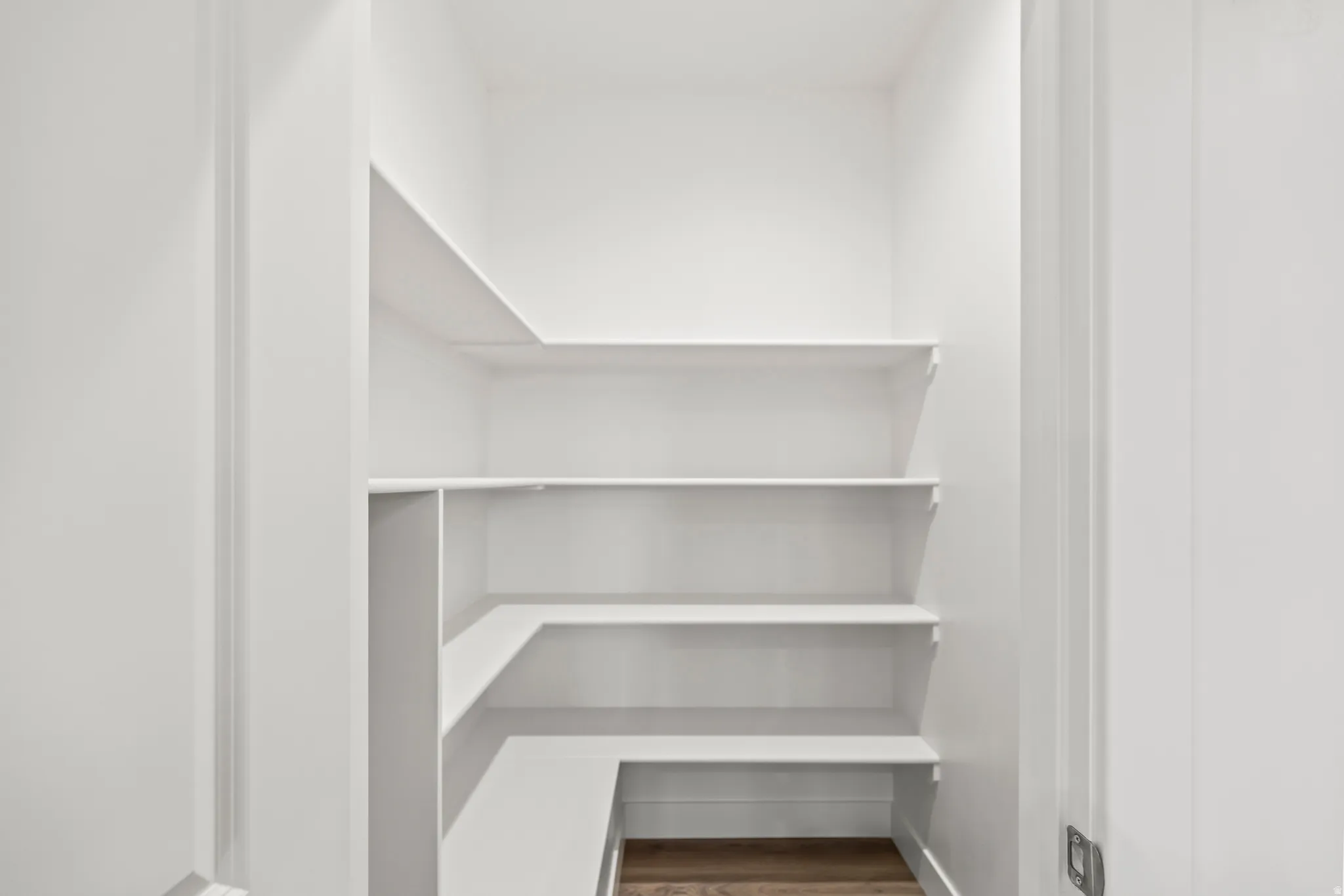 Walk-in pantry with multiple white shelves and wood-finish flooring