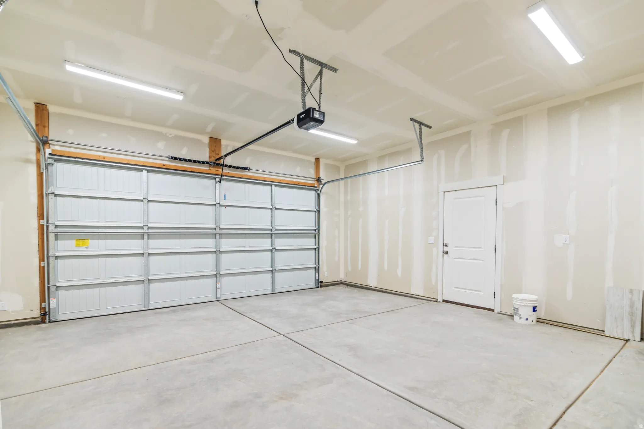 Spacious garage with a concrete floor, large overhead door, automatic opener, and a side entry door