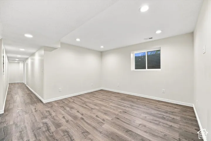 Spacious basement recreation room featuring wood-finish flooring, recessed ceiling lighting, and clean white walls