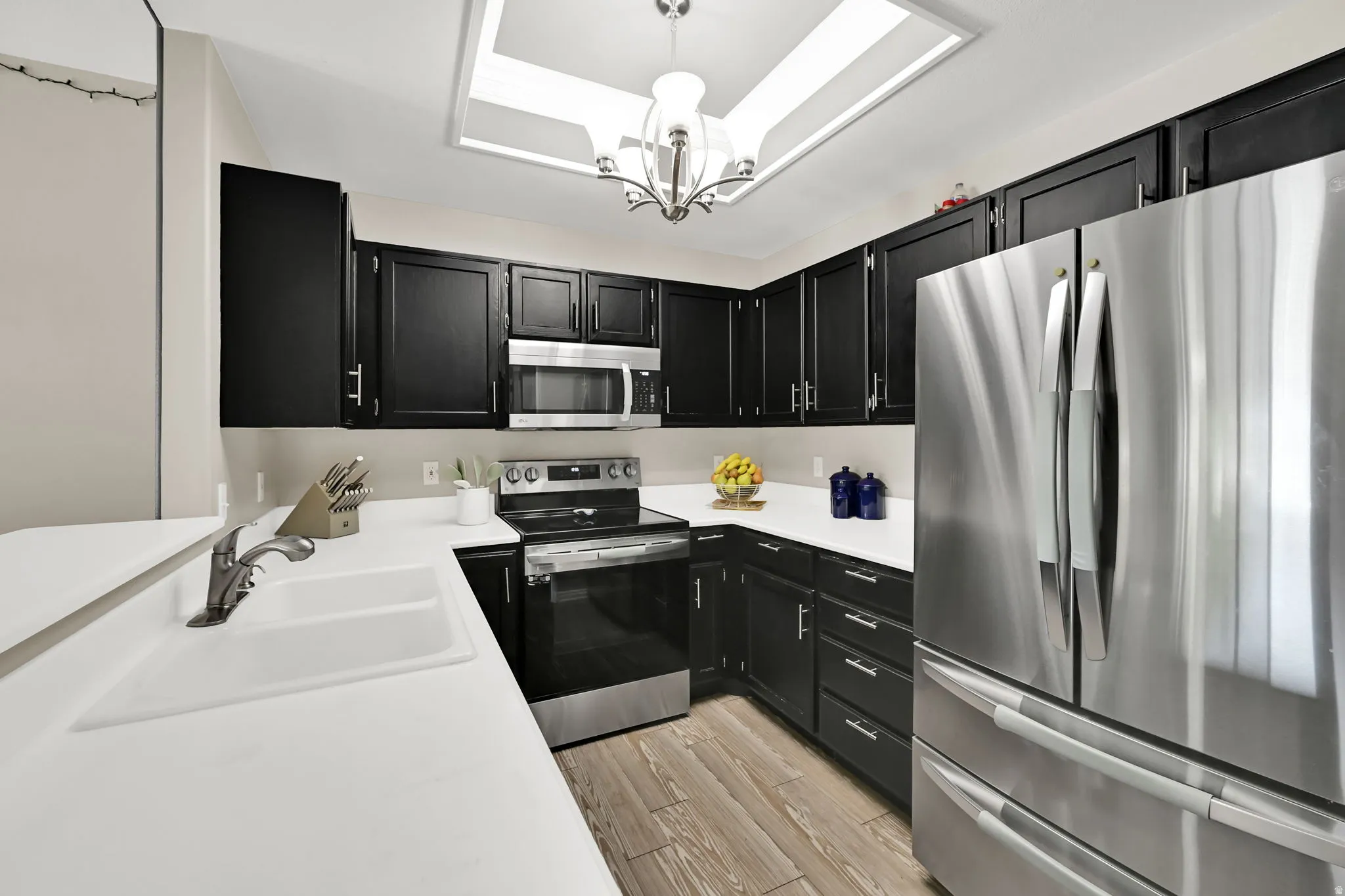 Kitchen featuring black cabinetry, white countertops, stainless steel appliances, and wood-finish flooring