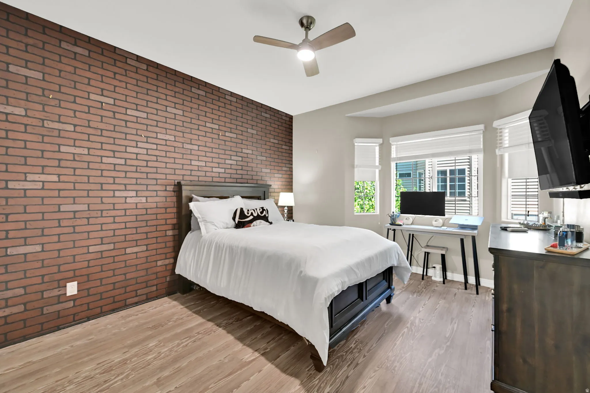 Accent brick wall, wood-finish flooring, ceiling fan, multiple windows with blinds, recessed lighting