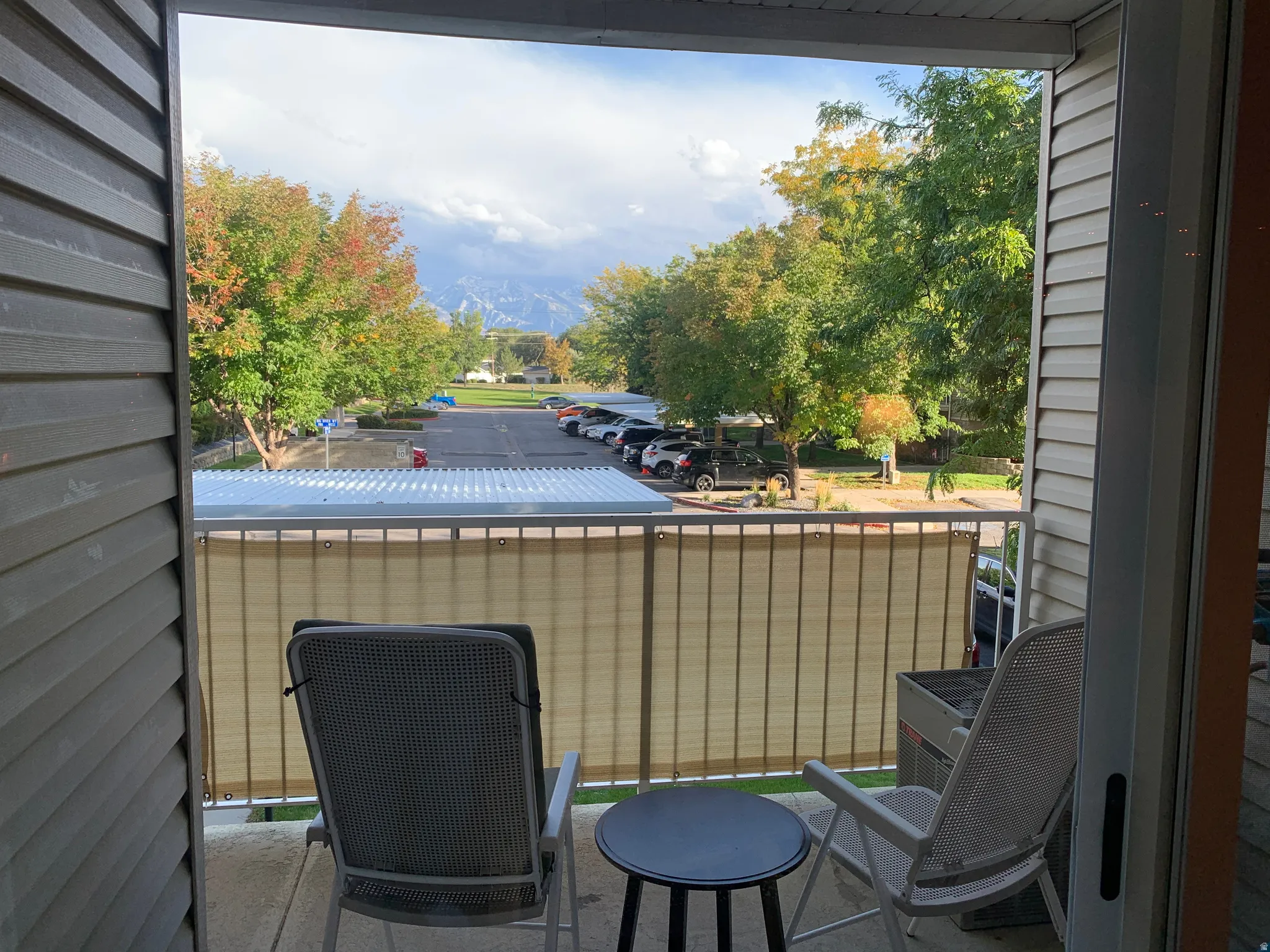 Balcony with metal railing, concrete flooring, and surrounding mature trees