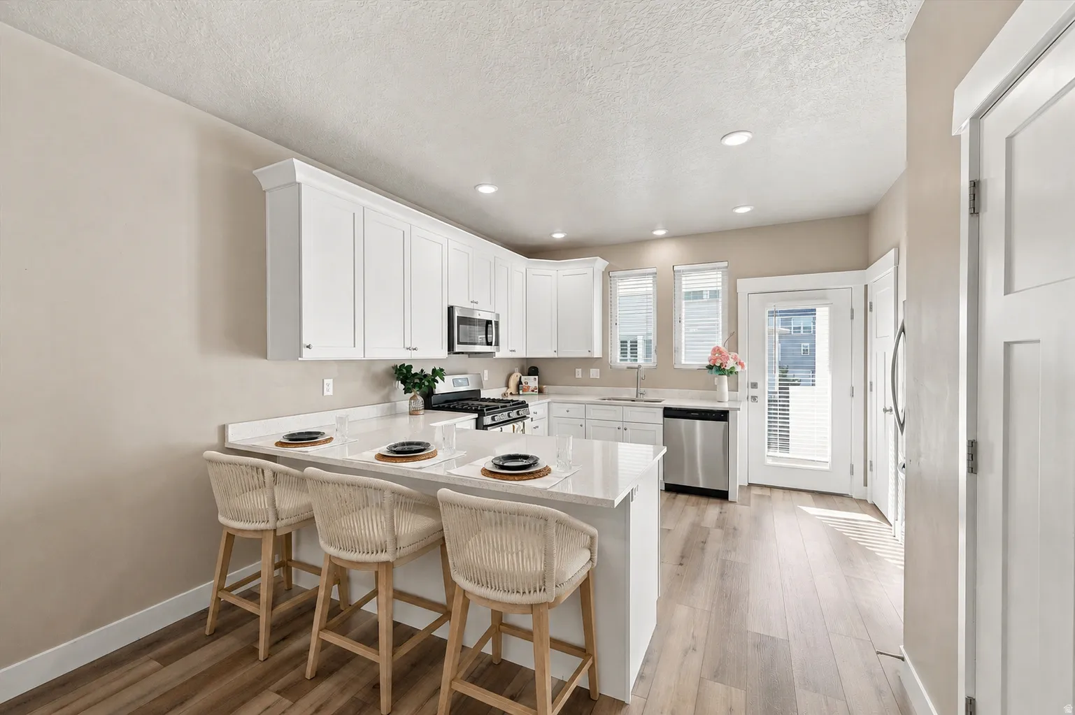 Beautiful kitchen with a lot of light. White cabinetry, stainless steel appliances, wood-finish flooring, recessed lighting, and a kitchen island with seating