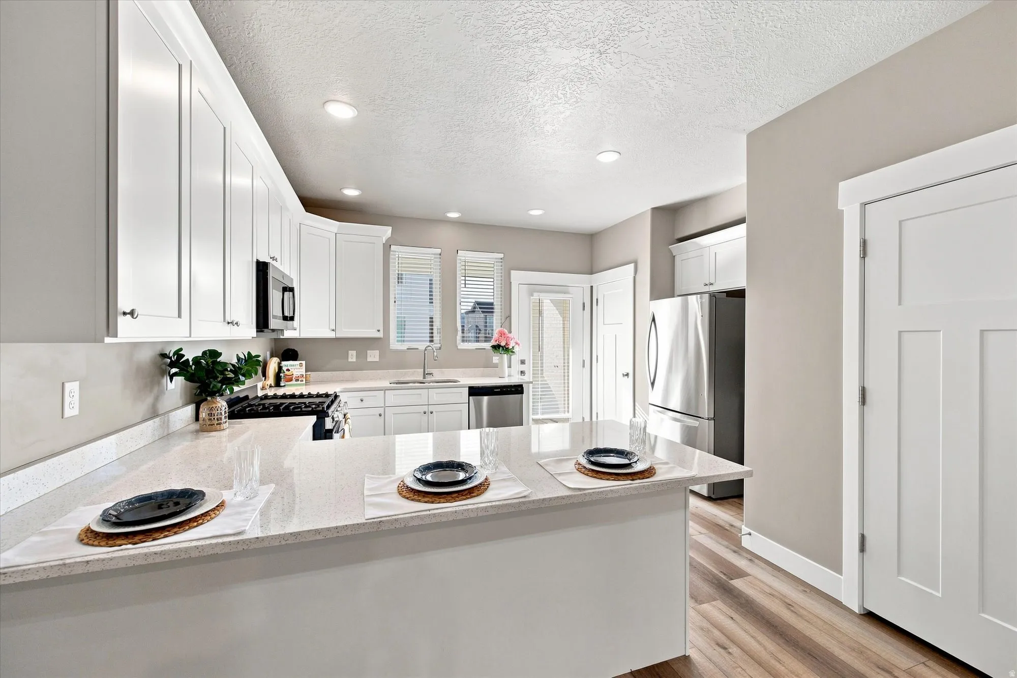 White shaker cabinetry, light-toned countertops, stainless steel appliances, wood-finish flooring, and recessed lighting.