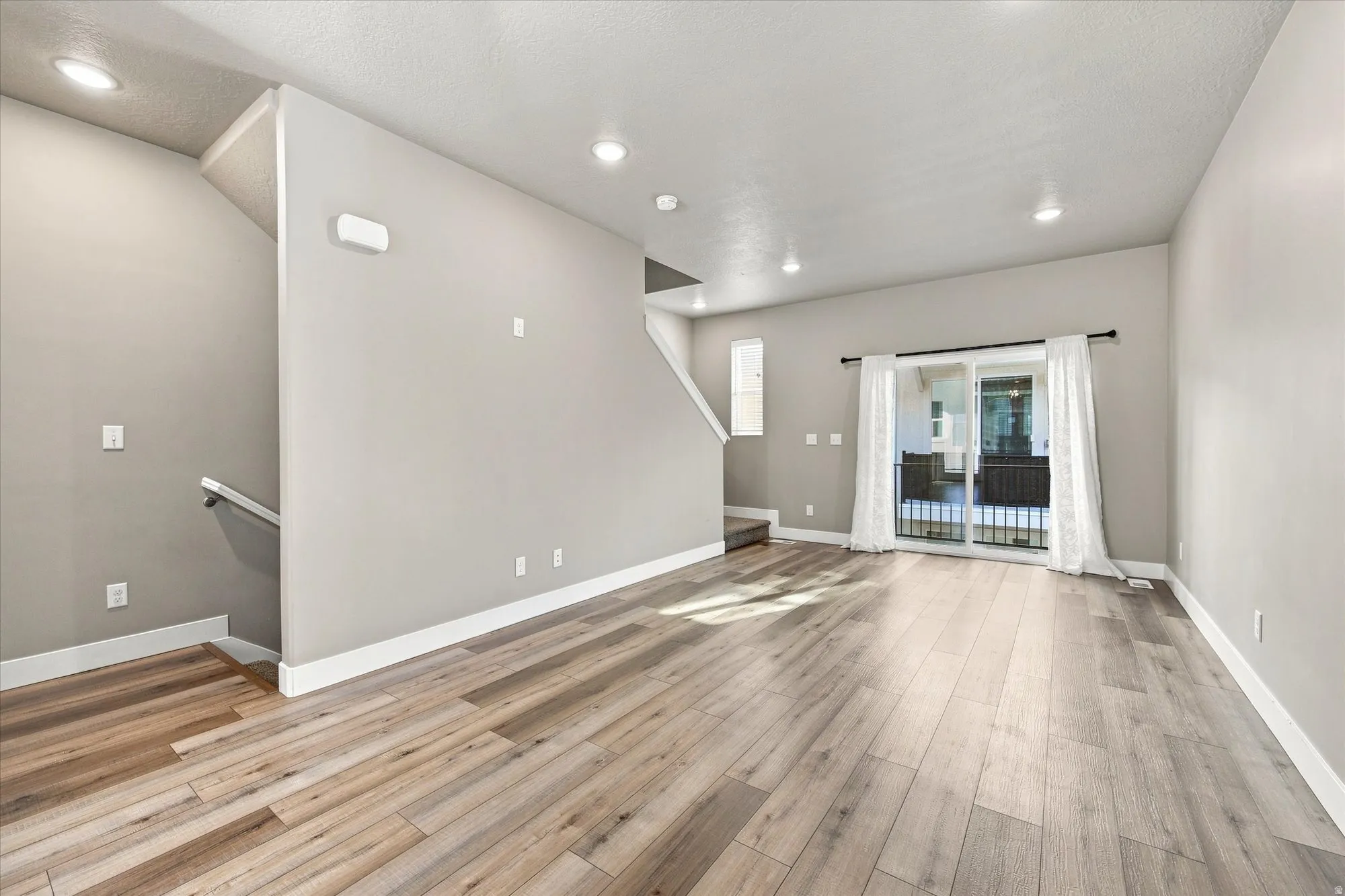 Spacious room featuring natural lighting wood-finish flooring, recessed ceiling lights, and a sliding glass door leading to an outdoor balcony.