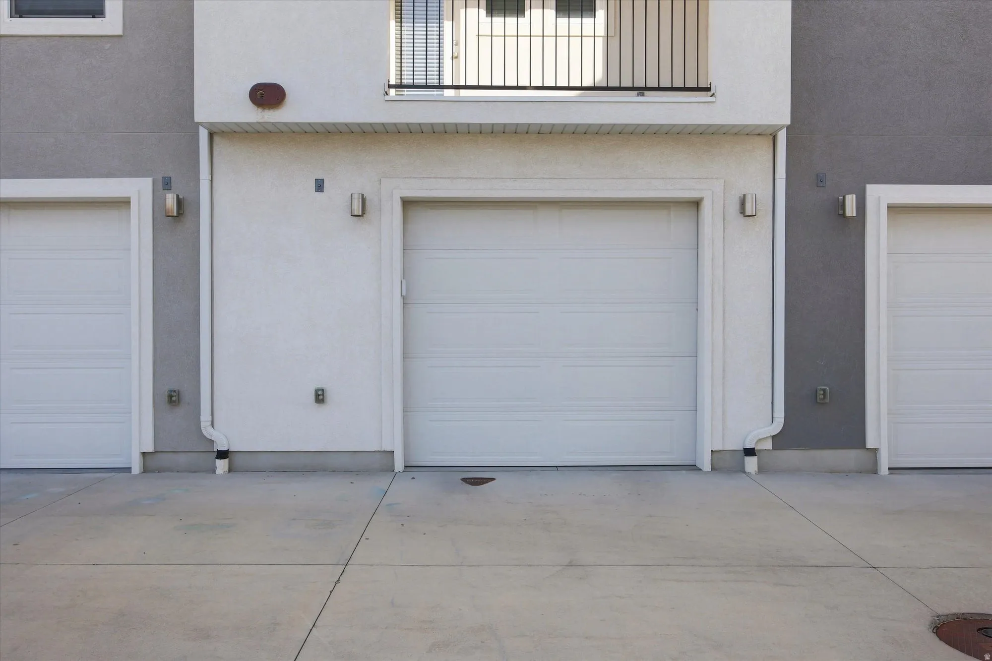 Three white panel garage doors, concrete drive, and modern exterior lighting fixtures. Extra long garage.