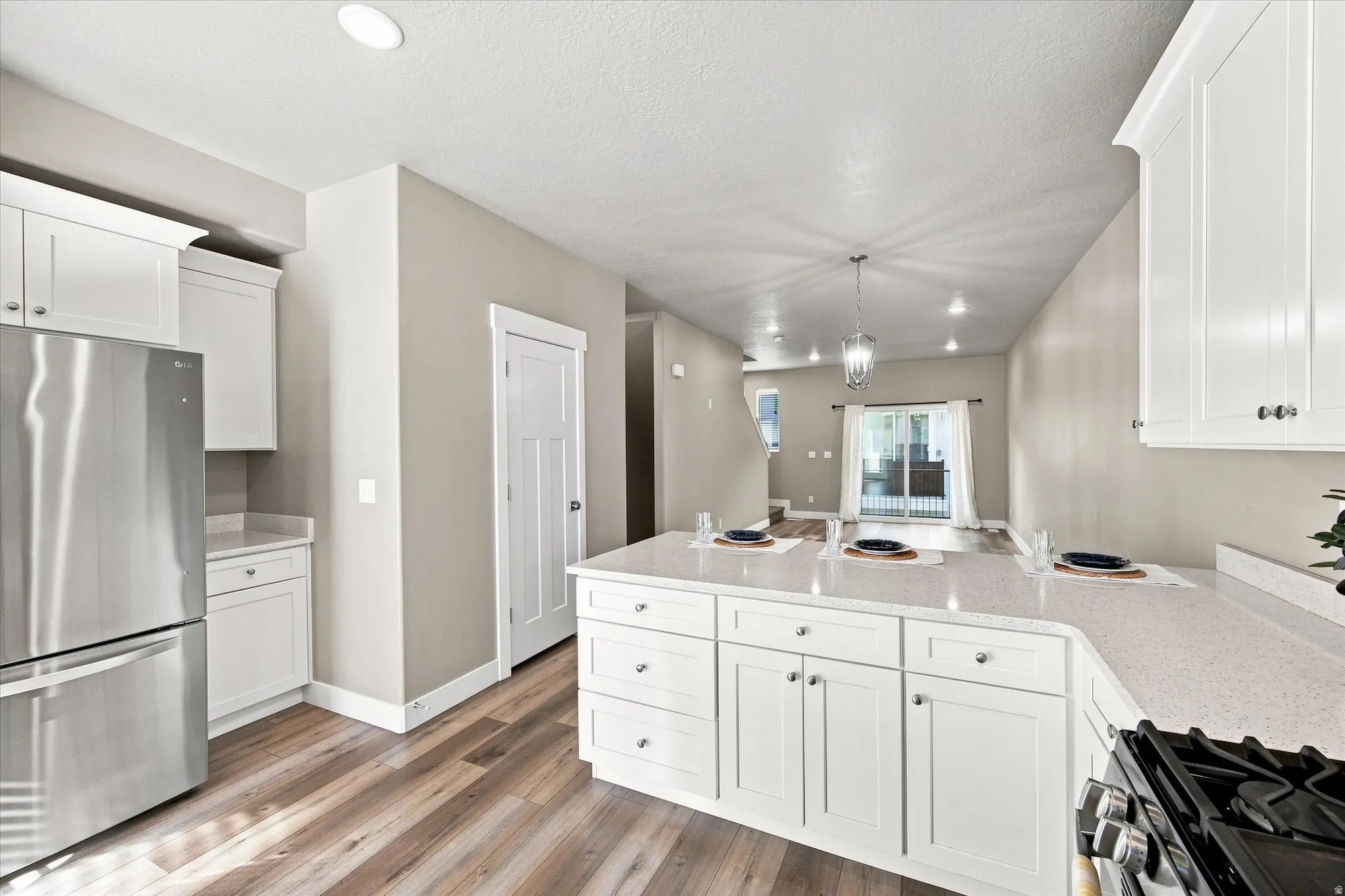 Modern kitchen with natural light, featuring wood-finish flooring, white cabinetry, stainless steel appliances, and light-toned countertops.