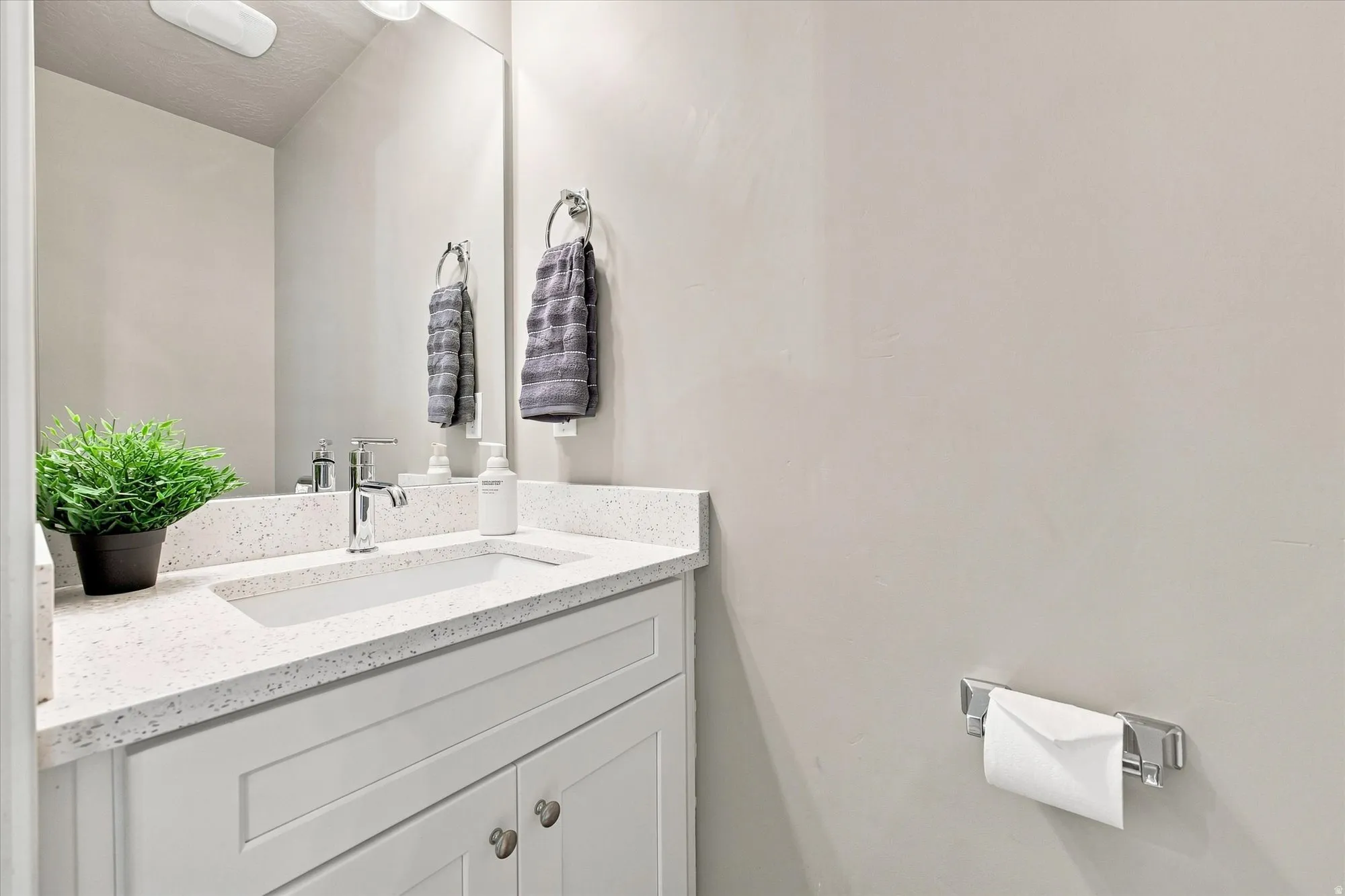 White vanity with shaker-style cabinetry, a built-in rectangular sink, and a speckled quartz countertop. Half bathroom off of family room area.