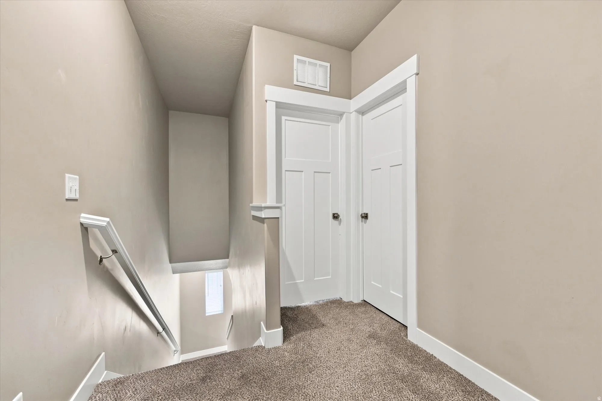 Neutral-toned walls with contrasting white trim, carpeted flooring, and a white handrail. Second floor landing.