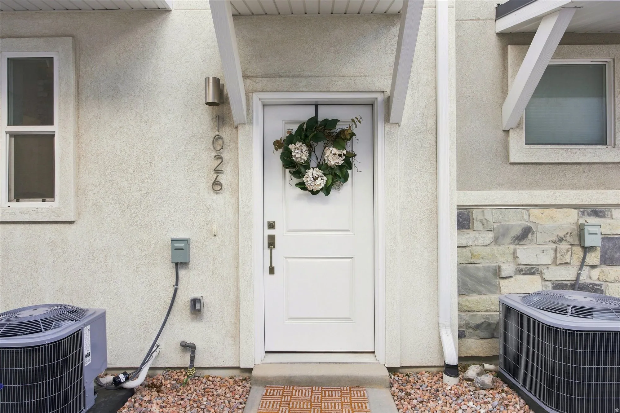 White paneled entry door with transom light, stucco exterior finish, and stone accent wall.