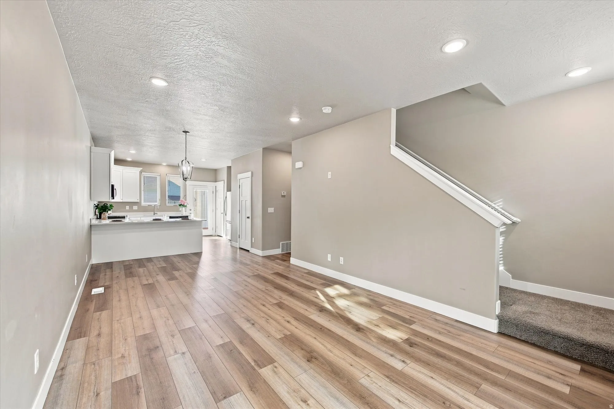 Wood-finish flooring, recessed lighting, white kitchen cabinetry, kitchen island with countertop, and carpeted staircase. Balcony off front and back.