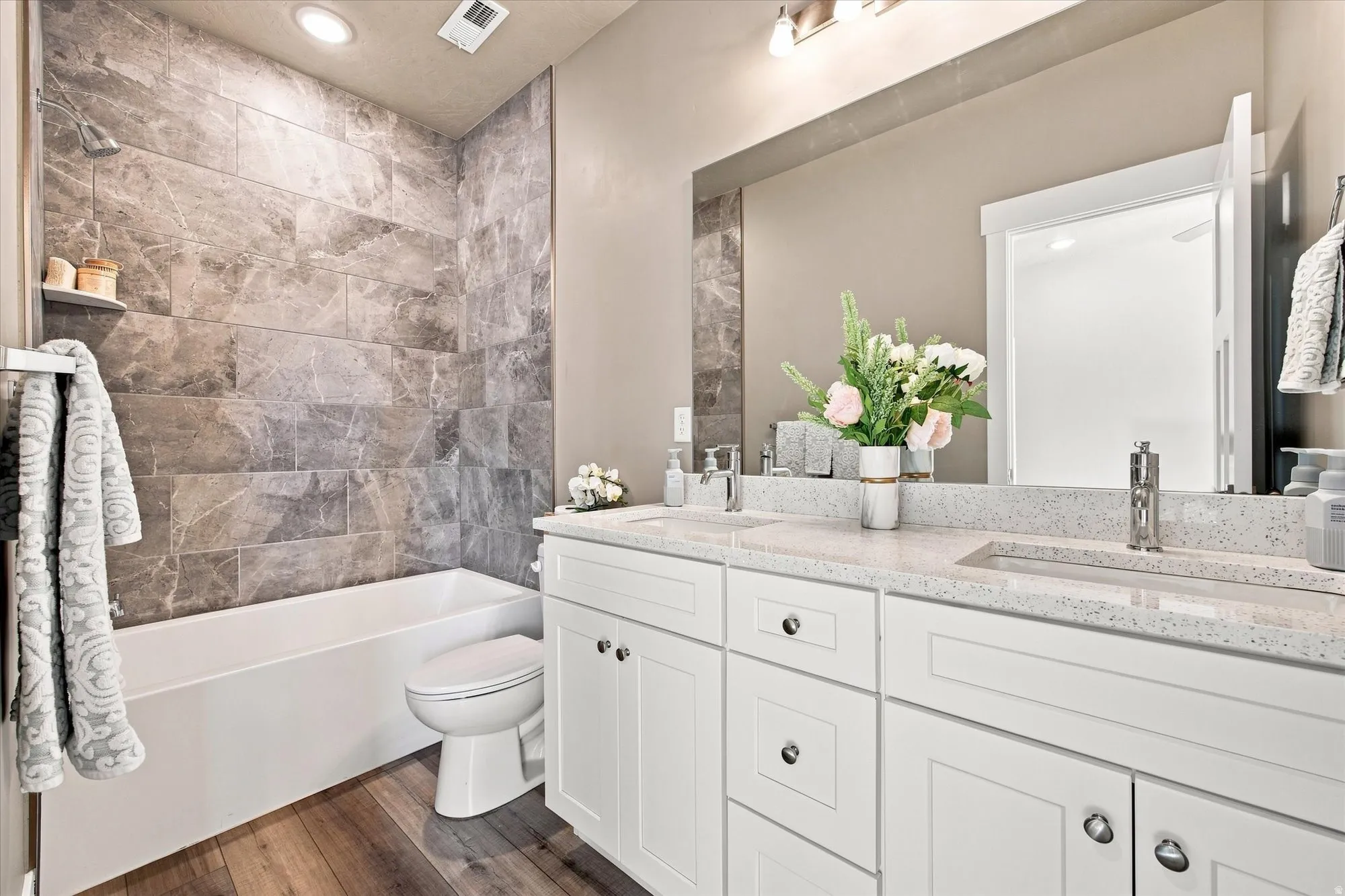 Owners bathroom. Dual sink vanity with white cabinetry and chrome hardware, a large mirror, a separate tub, a toilet, and wood-finish flooring