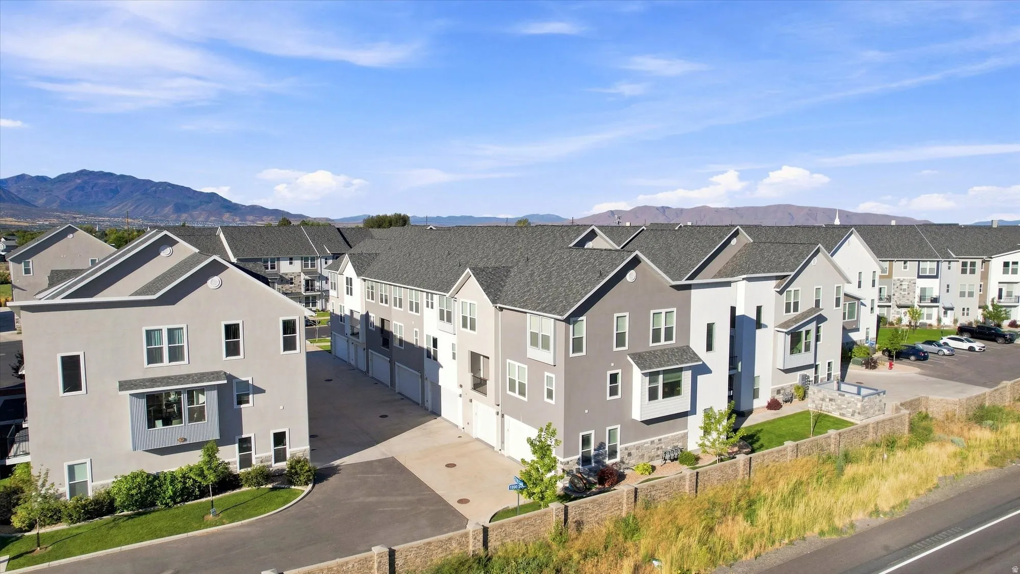 Modern townhome community featuring multi-story units, attached garages, and a paved parking area.