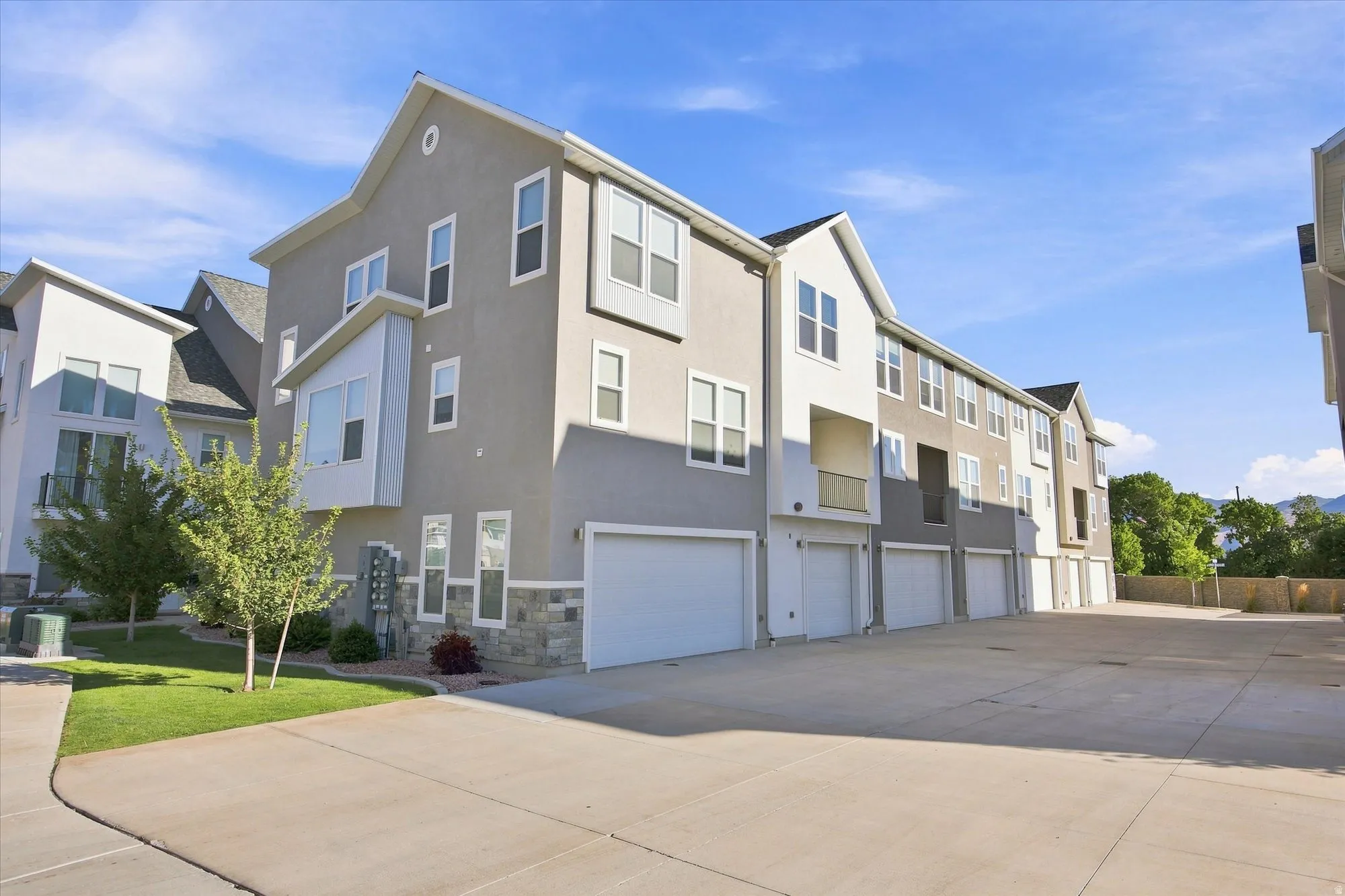 Multi-level exterior with stucco and stone accents, individual garage doors, and a prominent bay window.