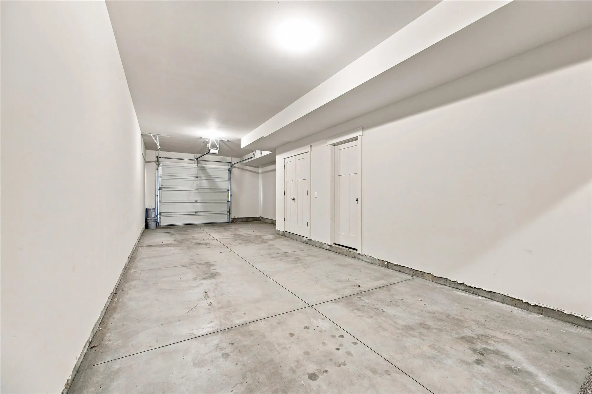 Attached garage with a concrete floor, overhead lighting, and two interior doors.