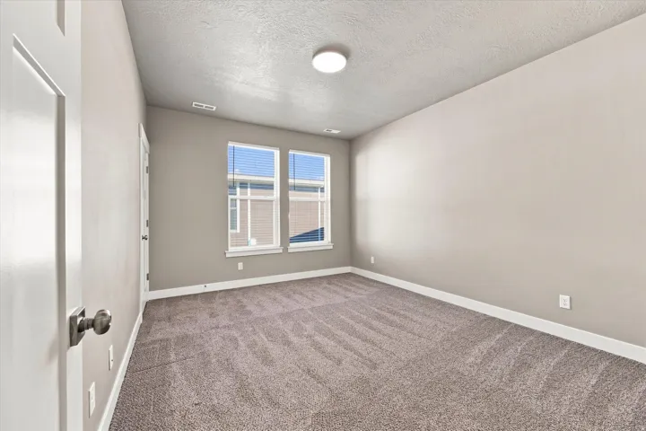 Large bedroom with new paint, textured carpeting, double windows with blinds, prominent ceiling light fixture, and white trim.