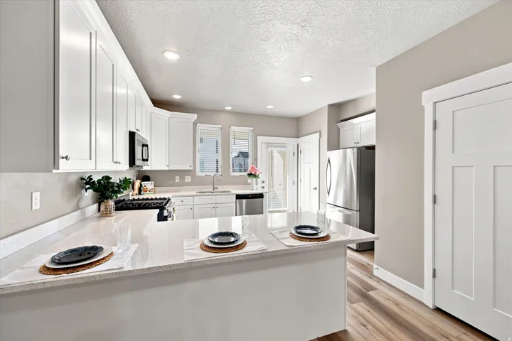White shaker cabinetry, light-toned countertops, stainless steel appliances, wood-finish flooring, and recessed lighting.