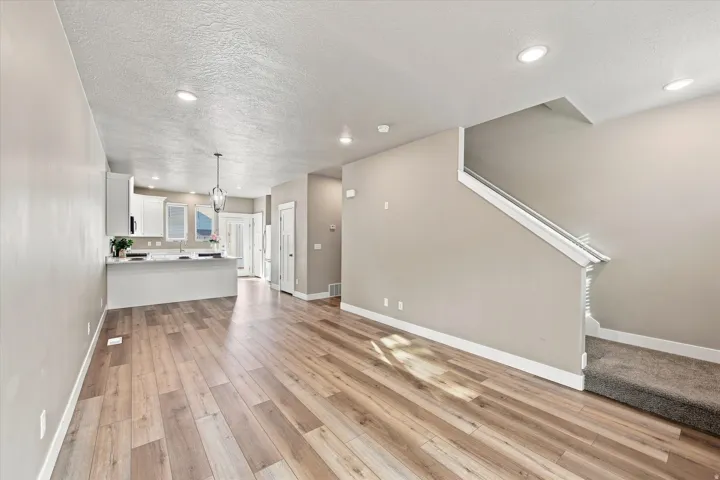 Wood-finish flooring, recessed lighting, white kitchen cabinetry, kitchen island with countertop, and carpeted staircase. Balcony off front and back.