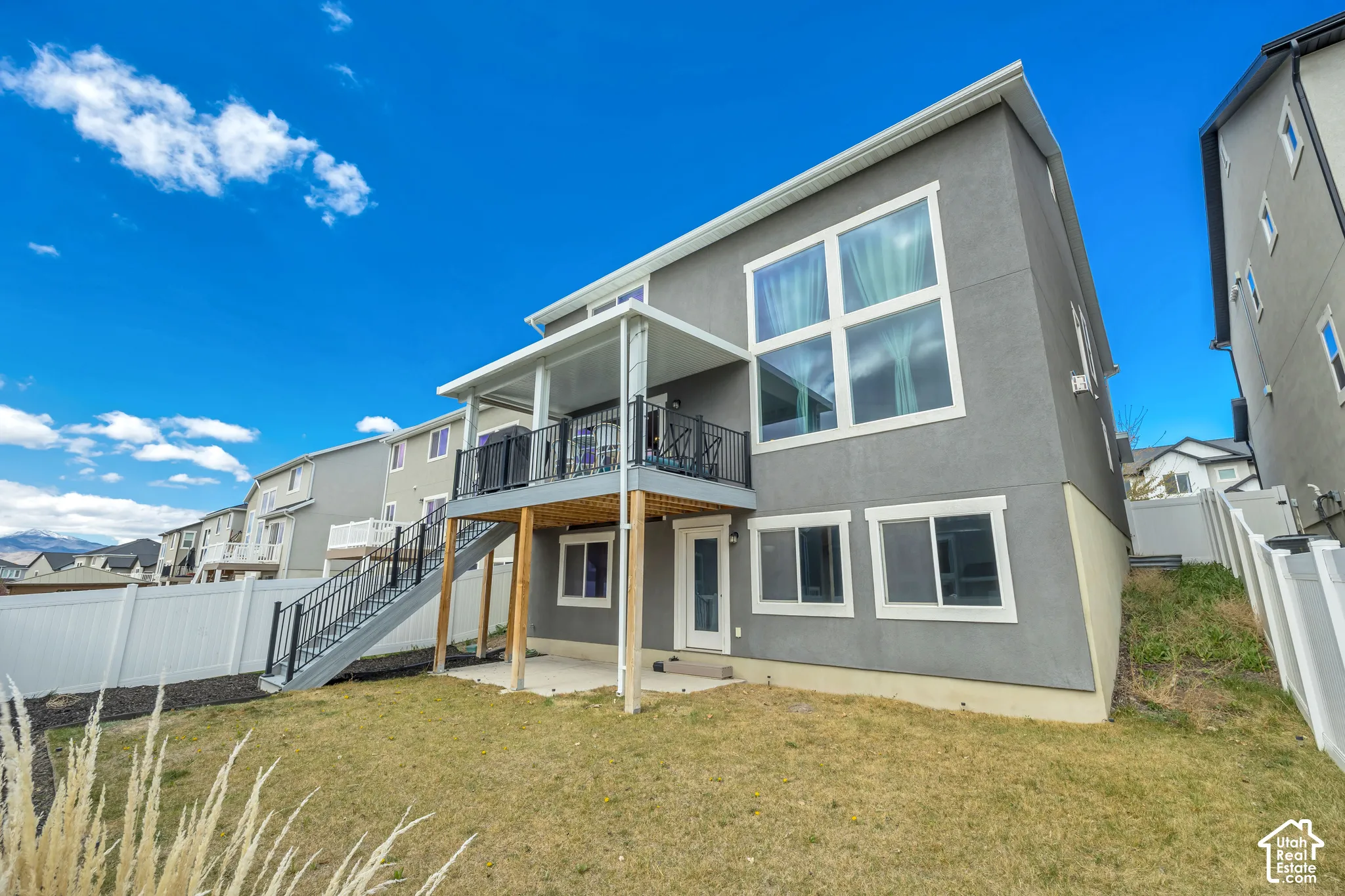 Rear exterior featuring a covered deck with black railings, a ground-level patio, and multiple windows