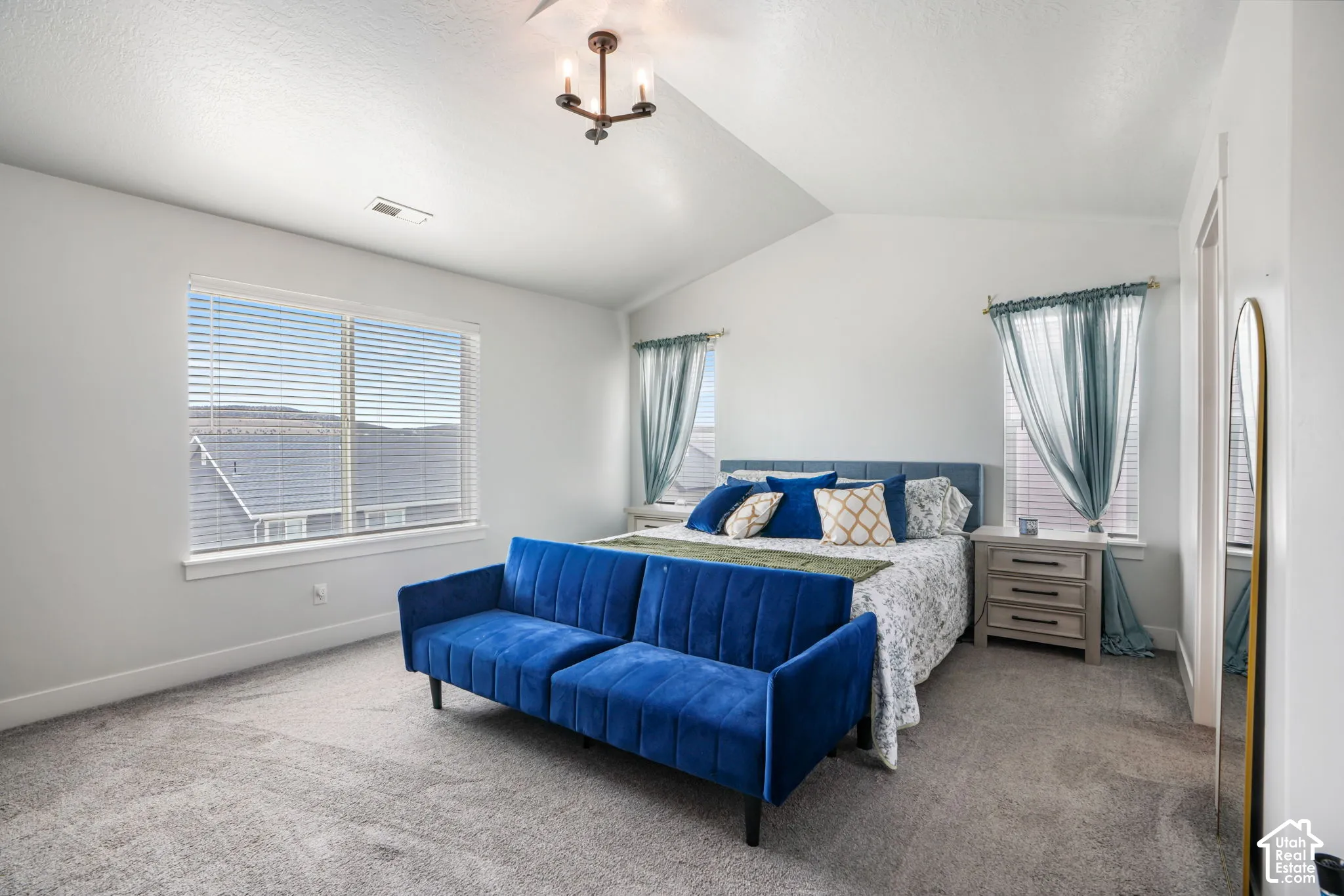 Vaulted ceiling, ceiling-mounted light fixture, light-toned wall paint, large window with blinds, and carpeted flooring