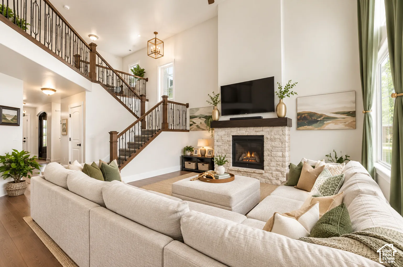 Double-height ceiling, fireplace with natural stone veneer and timber mantel, wood-finish flooring, and staircase featuring decorative iron balusters with wood handrails