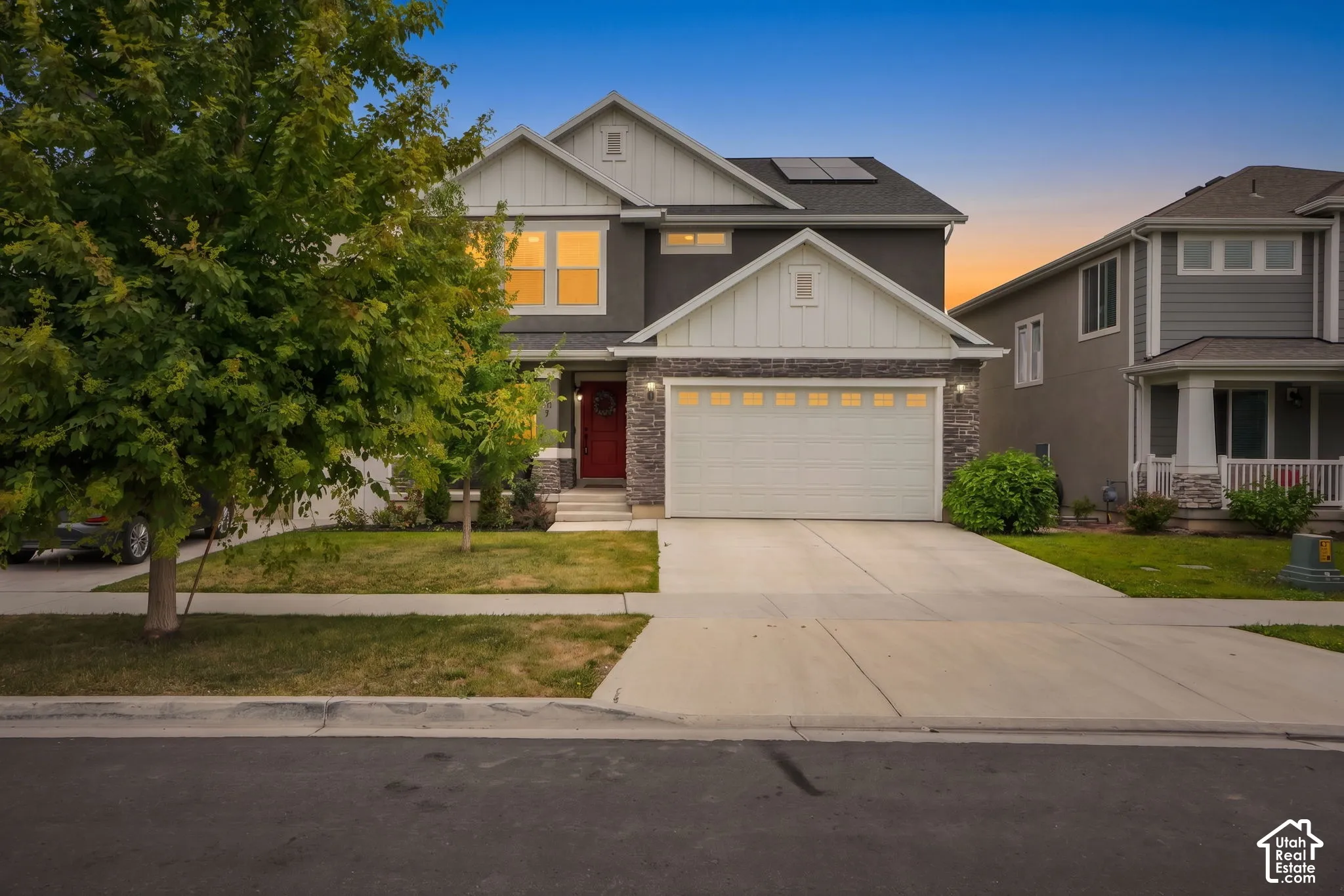 Modern facade featuring a stone accent, a two-car garage, a vibrant red entry door, and solar panels