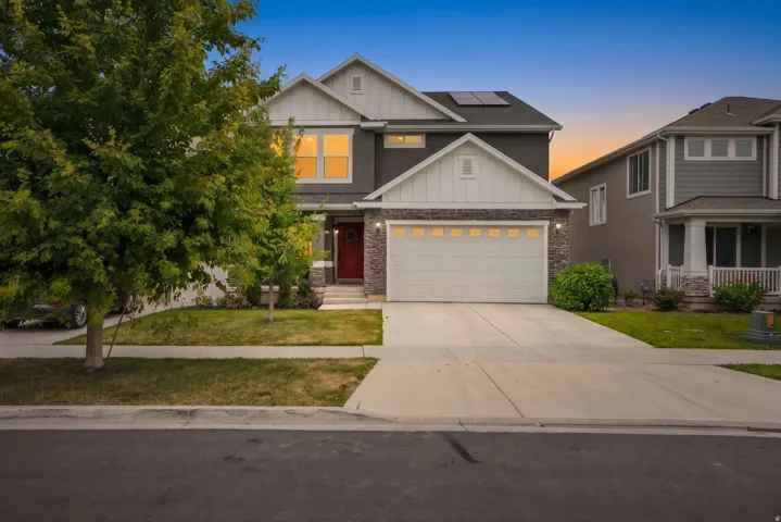 Modern facade featuring a stone accent, a two-car garage, a vibrant red entry door, and solar panels