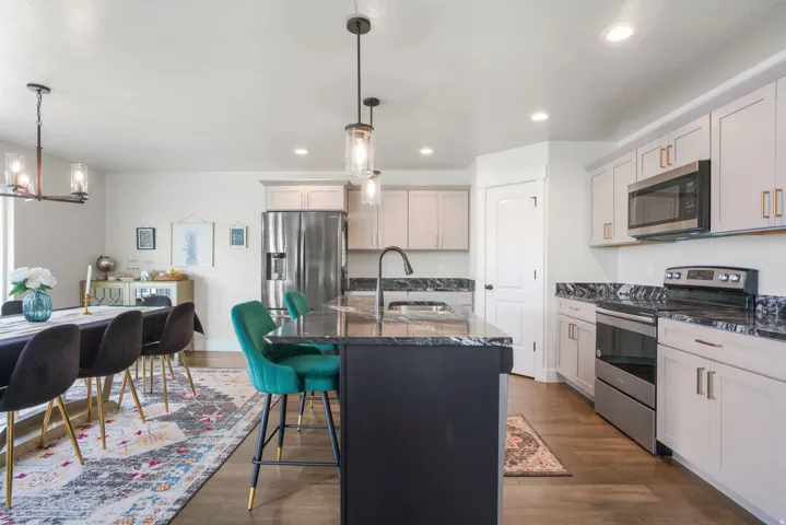 Kitchen featuring stainless steel appliances, dark stone countertops, light cabinetry, and an island with pendant lighting