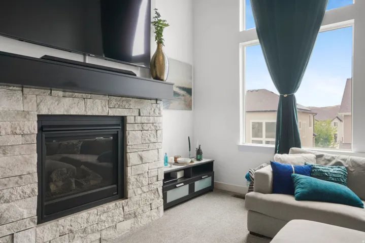 Stacked stone fireplace with a black mantel, high ceilings, and tall windows