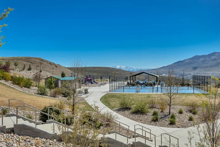 Community park with concrete pathways, a playground, covered sports courts, and mountain scenery