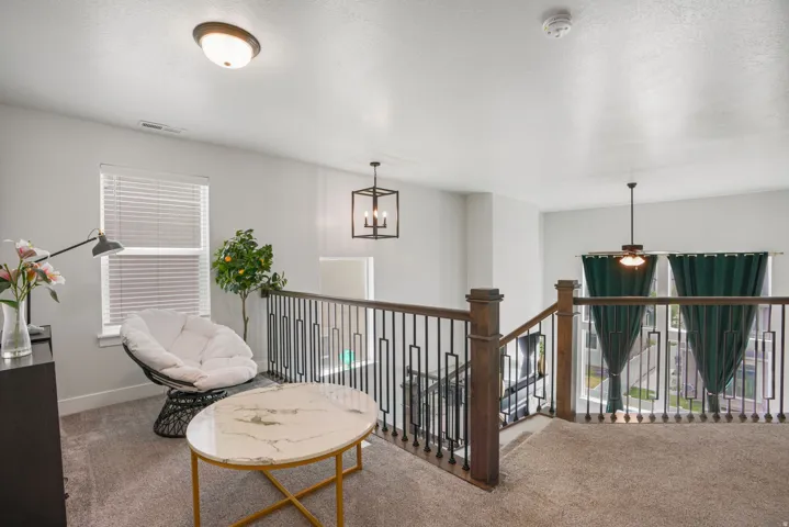 Carpeted loft area featuring a dark wood newel post, metal balusters, and a contemporary cage pendant light fixture