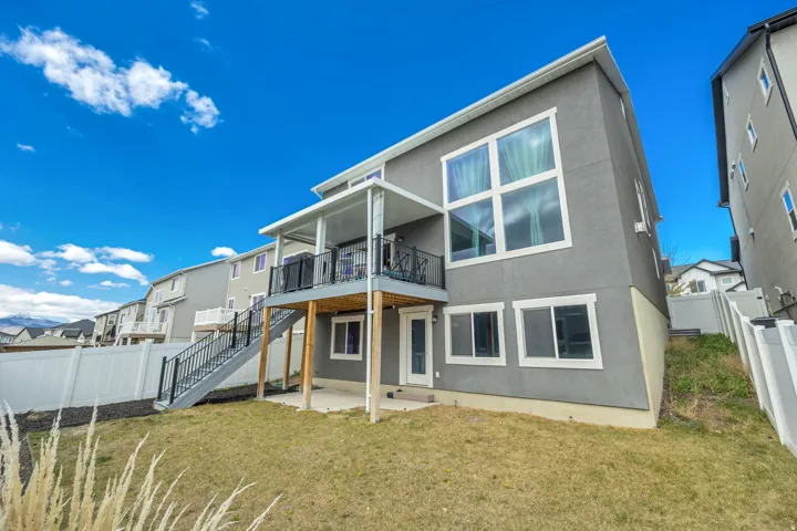 Rear exterior featuring a covered deck with black railings, a ground-level patio, and multiple windows