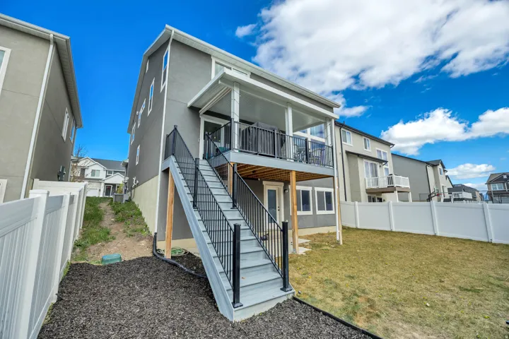Upper-level covered patio with railing, exterior staircase with railing, lower-level exterior door, and multiple windows