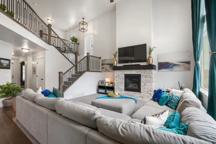 Open-concept living area featuring a two-story ceiling, stone-clad fireplace with a dark wood mantel, and wood-finish flooring