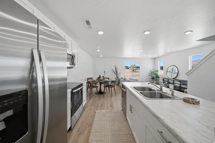 Stainless steel appliances, wood-finish flooring, recessed lighting, white cabinetry, and a double basin sink