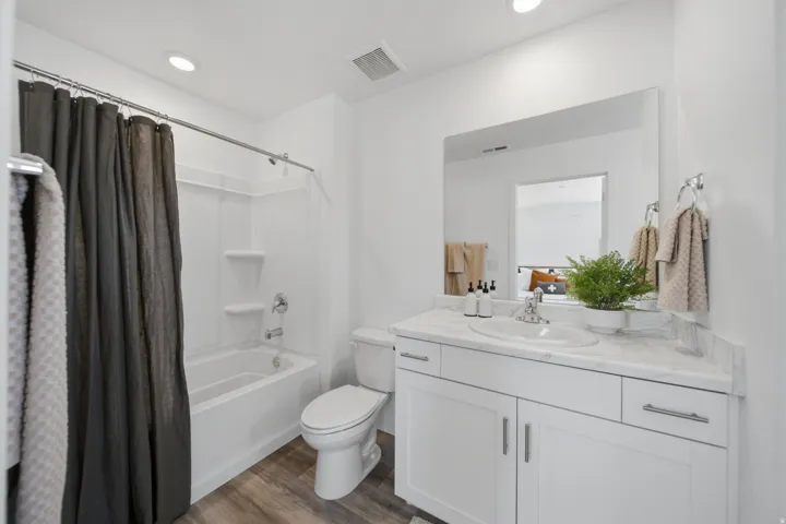Full bathroom featuring a white vanity with an integrated sink, a vanity mirror, a toilet, a bathtub with a shower, and wood-finish flooring