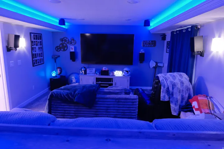 Recessed ceiling lighting, wall-mounted sconces, ceiling-mounted speakers, and a large wall-mounted display
