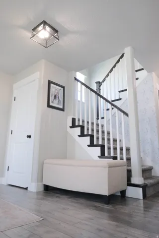 Bright foyer with elegant staircase featuring black metal railings and white balusters, wide-plank wood-finish flooring, recessed ceiling lighting, and clean white walls with crisp architectural detailing
