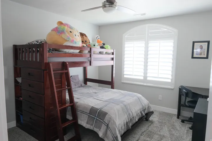Arch-top window with white plantation shutters, neutral gray wall paint, gray textured carpeting, and a ceiling fan with integrated lighting
