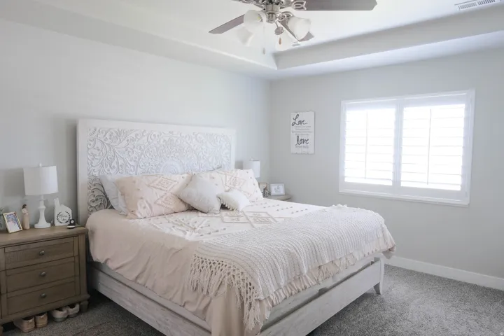 Tray ceiling with a ceiling fan, dual windows with plantation shutters, light gray wall finishes, and gray carpet flooring