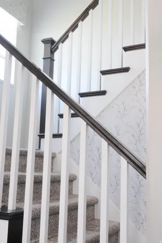 Staircase featuring dark wood-finish handrails, white balusters, carpeted treads, and patterned wall covering