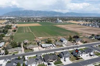 Aerial perspective showcasing residential properties, expansive agricultural fields, and distant mountainous terrain under a cloudy sky