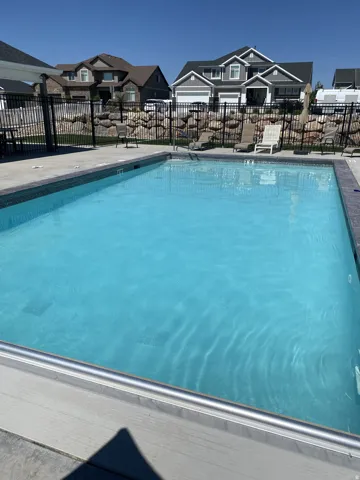 Outdoor swimming pool with a concrete surround, enclosed by a black metal fence