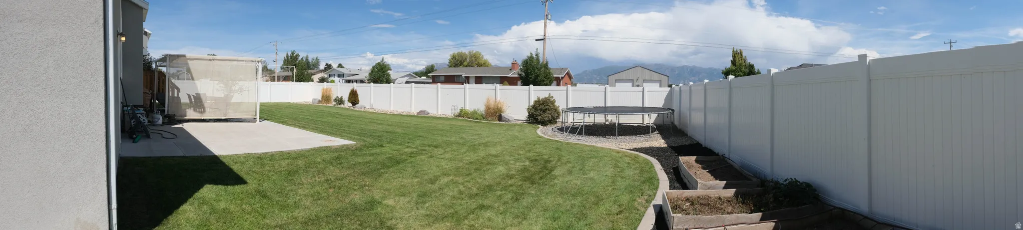 Expansive backyard featuring a manicured lawn, concrete patio, white privacy fencing, and raised garden beds