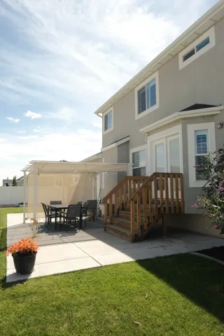 Two-story stucco exterior, wood deck with stairs, covered patio area, concrete patio, and a manicured lawn